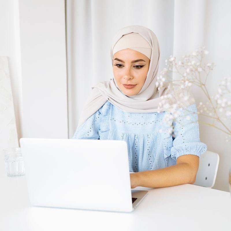 Student in hijab attending an online Quran class on a laptop