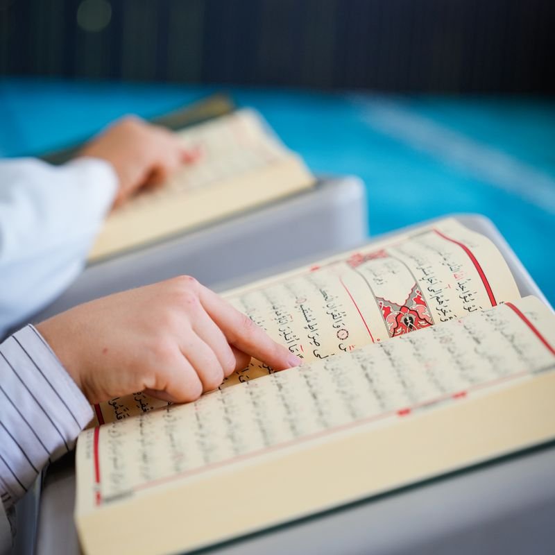 Student tracing Quran verses with a finger while learning Tajweed